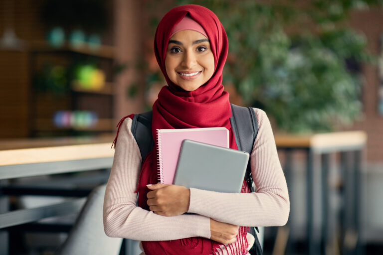Happy young muslim woman student in hijab with backpack, digital tablet and books posing at cafe, beautiful middle-eastern lady studying at cafeteria while having lunch break at university, copy space