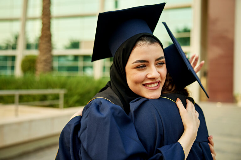 Smiling graduate female student embracing friend wearing mortarboard during convocation